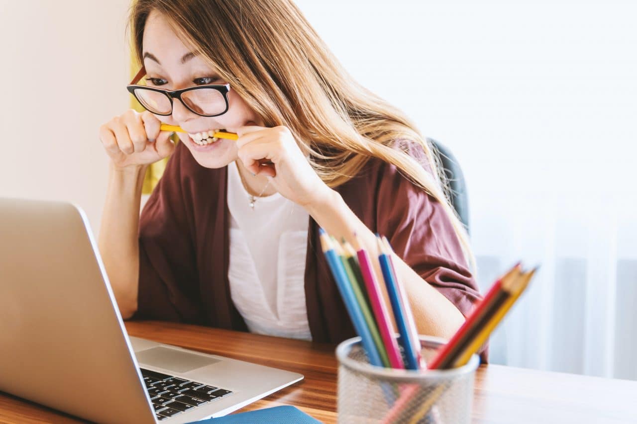 Woman biting on a pencil while looking at a laptop