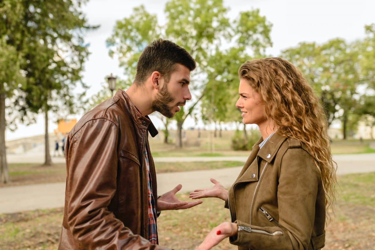 man and woman facing each other arguing in a park 