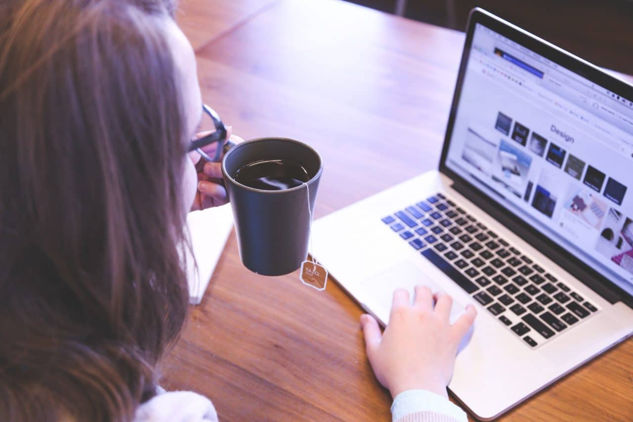 Woman holding a cup of tea while working on a laptop