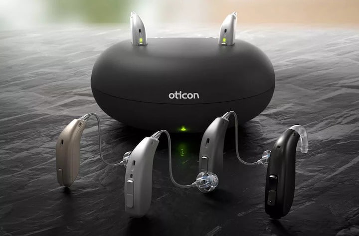 Oticon hearing aids in front of a charging base