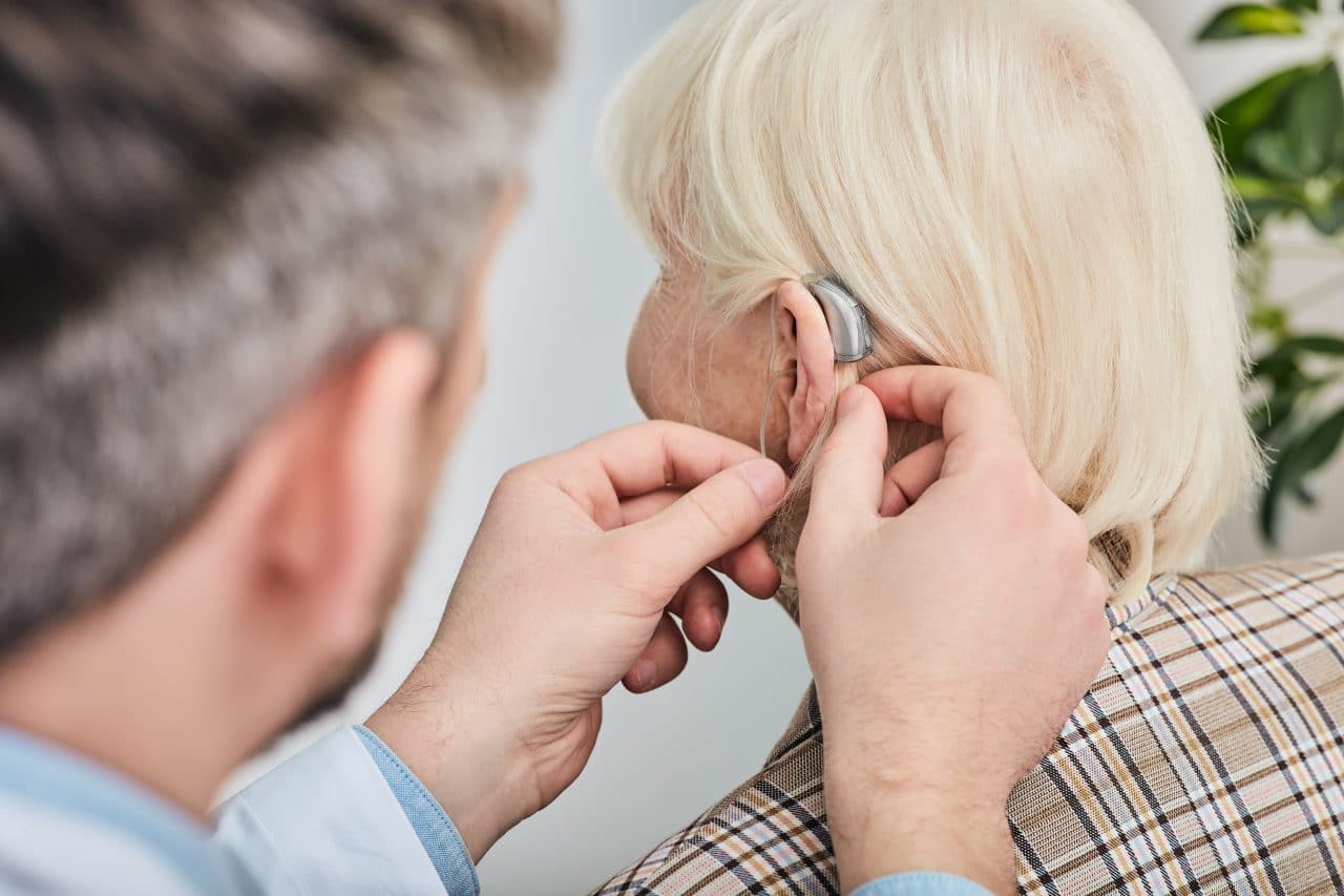 Audiologist fitting a woman with hearing aids.