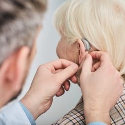 Audiologist fitting a woman with hearing aids.