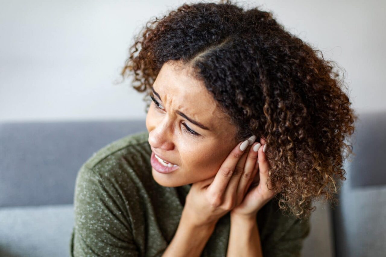 Woman experiencing ear pain, holding her hands to her ears.
