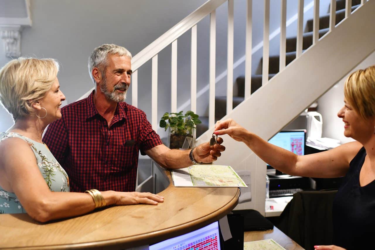 A Caucasion couple checking in a reception being friendly with the receptionist.  They are getting the room key from her.