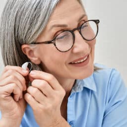 Smiling woman putting in a hearing aid